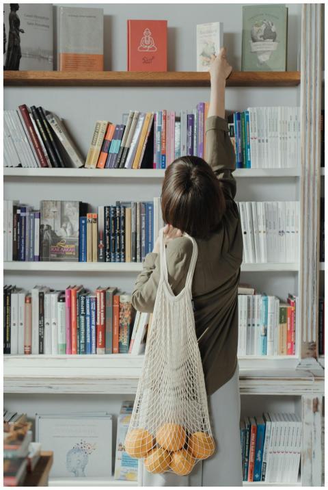 Female shopper reaching for a book on a high shelf