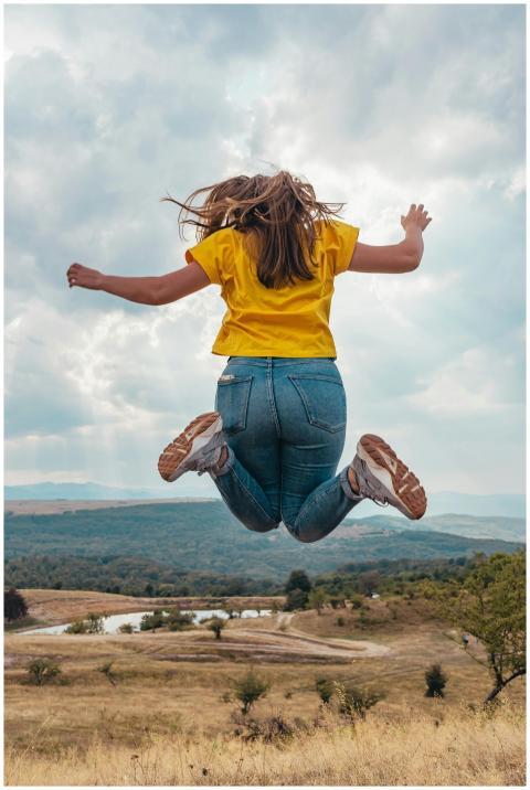 A woman in casual wear leaps joyfully in a scenic