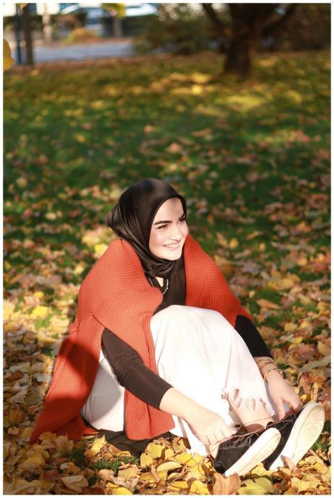 Smiling woman in hijab enjoying autumn leaves in t