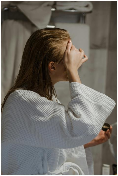 Side view of a woman applying a facial mask in a b