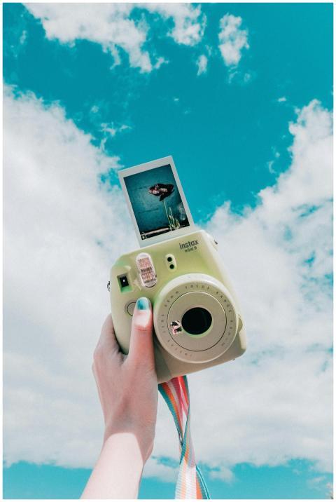 Hand holding an instant camera with a sky backgrou