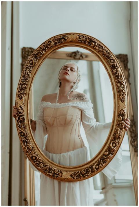 Woman gazing in an ornate oval mirror with a vinta