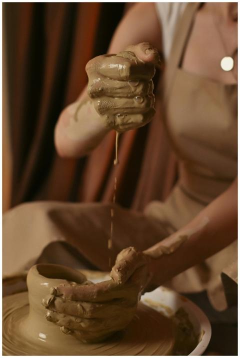 Hands expertly shape wet clay on a pottery wheel,