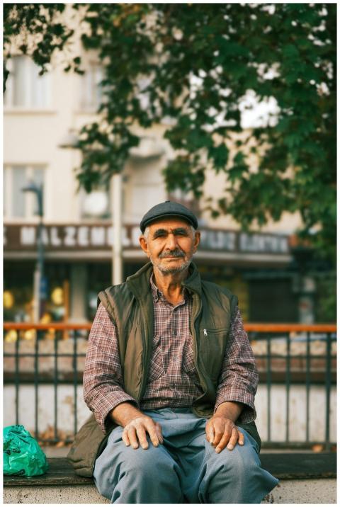 Elderly man sitting on a bench in an urban park wi