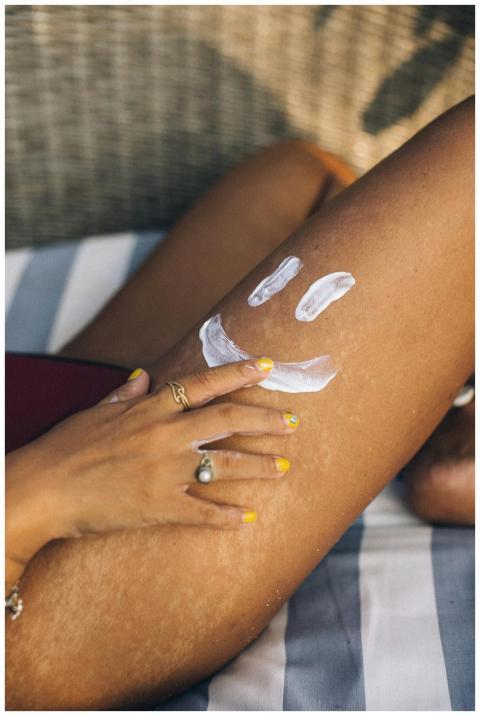 Close-up of a hand applying sunscreen on a leg wit