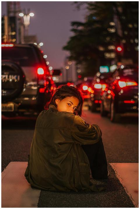 A young woman sits on a zebra crossing at night, s
