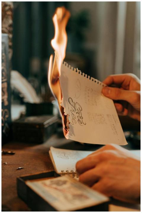 A close-up of hands holding a burning note with ar