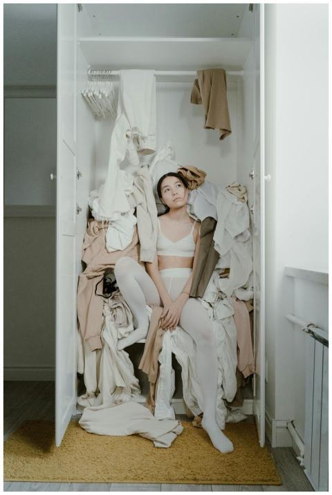 A contemplative woman sits surrounded by clothes i