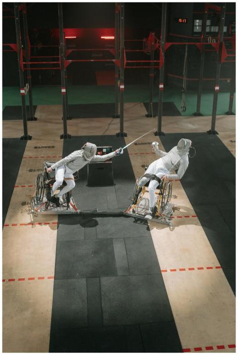 Two athletes in wheelchairs engage in a fencing ma