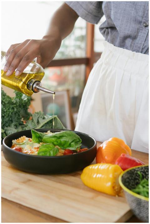 Person drizzles olive oil over fresh vegetable sal