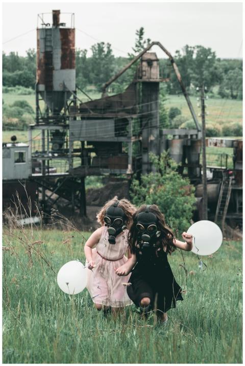 Two children in gas masks run with balloons near a