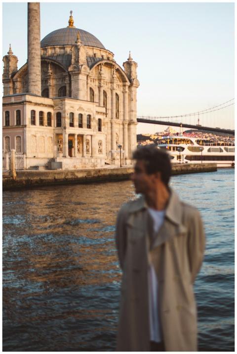 A man stands by the water with the historic Ortakö