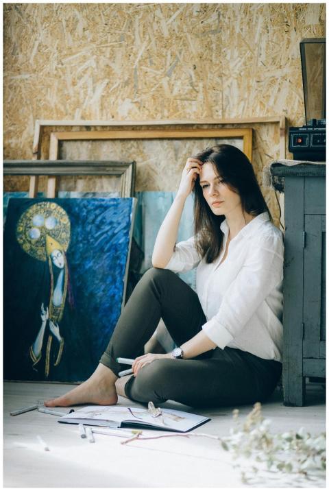 A woman sitting in an art studio, surrounded by pa