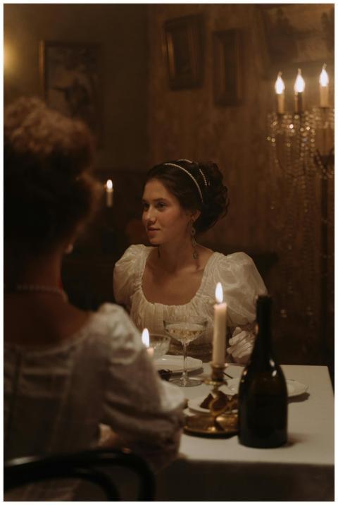 A woman in 19th-century attire at a candlelit dinn