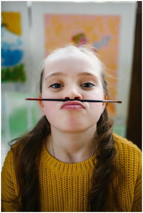 Young girl making a funny face with paintbrush as