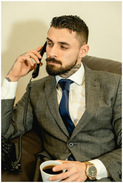 A bearded man in a gray suit sits in an office mak