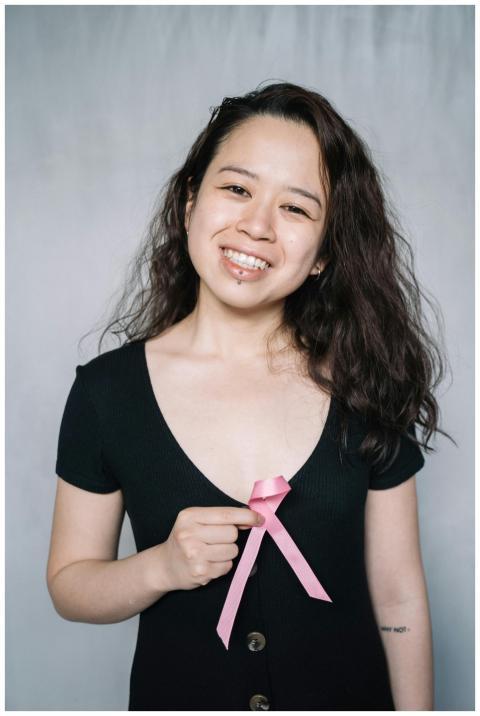 A smiling woman holding a pink ribbon symbolizing