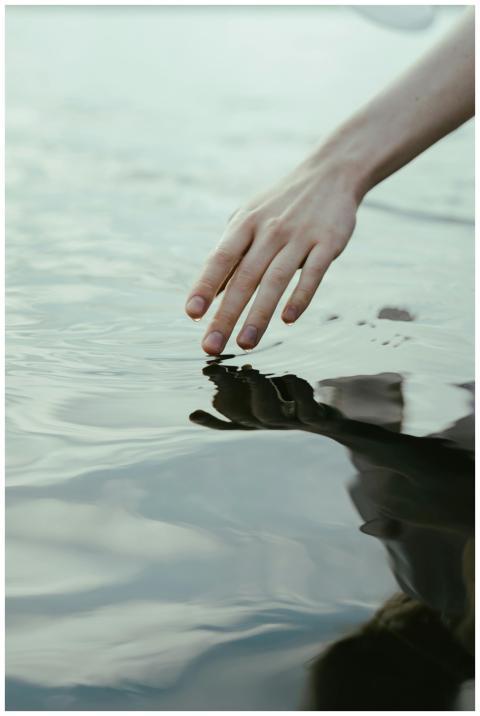 Close-up of a hand gently touching water with a re