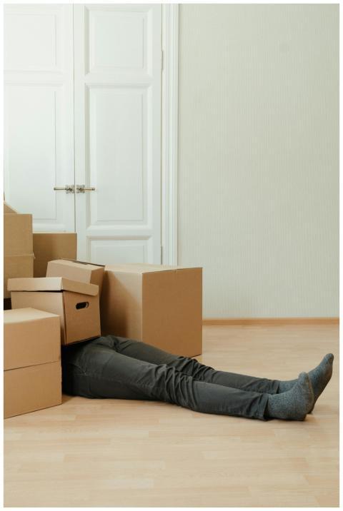 Man lying tired under cardboard boxes in an empty