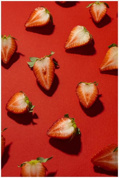 Vibrant sliced strawberries on a red surface, high