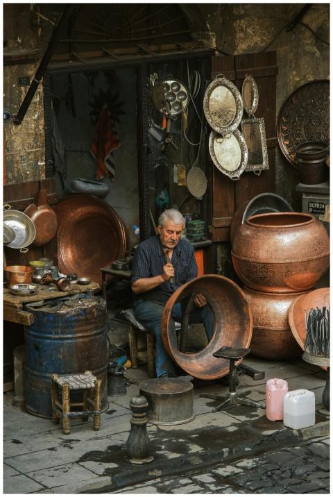 An artisan skillfully crafts copperware outside a