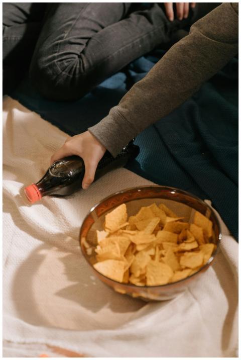 Hand reaching for soda bottle near bowl of chips o