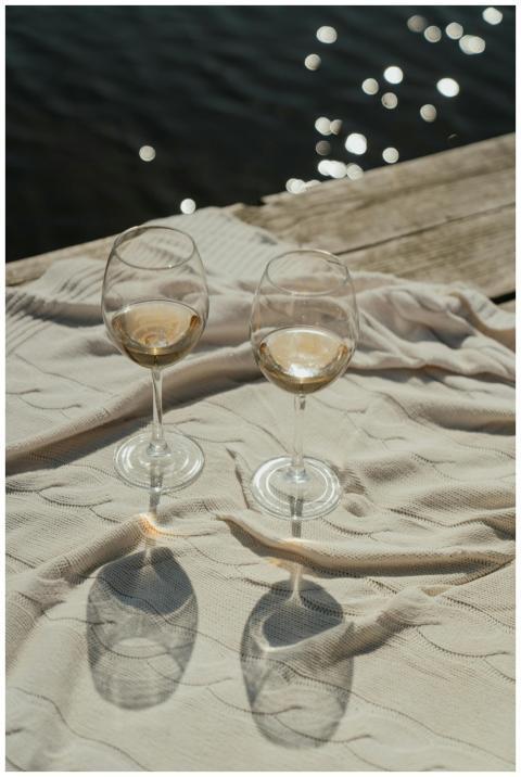 Two wine glasses on a blanket by a sunny lakeside