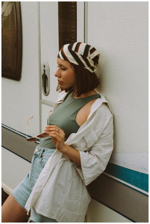 A stylish young woman leans against a camper weari