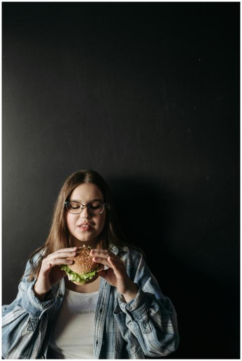 Brunette woman in glasses holding a hamburger agai