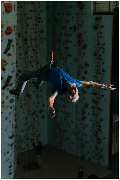 Senior man climbing in indoor facility on harness,