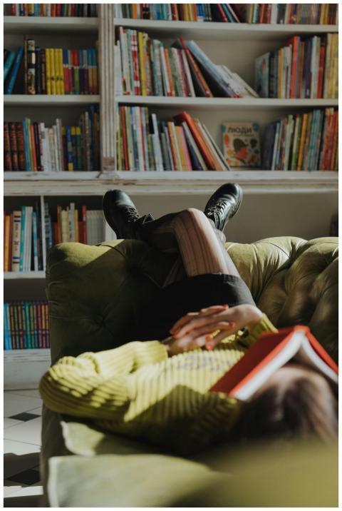 A woman in green rests with a book on a sofa in a