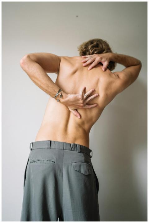 A shirtless man stretching his back indoors, showc