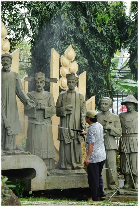 A person cleans large stone sculptures in a lush o