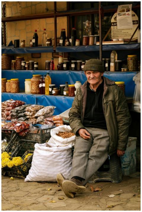 Portrait of an elderly vendor sitting by a colorfu