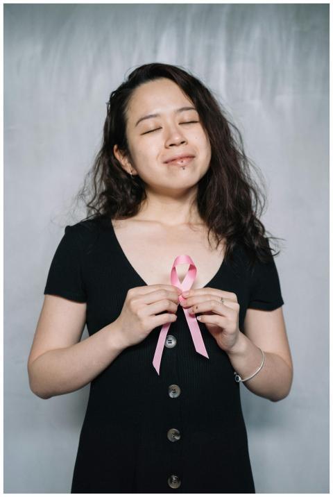 Smiling woman with eyes closed holding a pink ribb