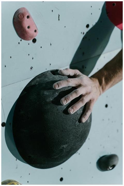 A climber's hand gripping a black climbing hold on