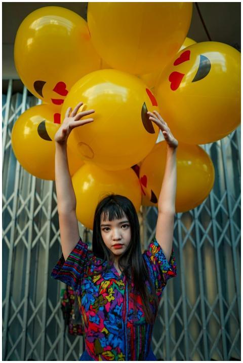 A young woman poses with bright emoji balloons aga