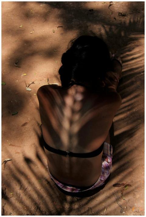 A woman sitting on a sunlit sandy ground with palm