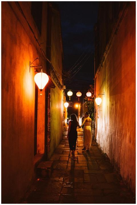 Two individuals walk hand in hand through a narrow