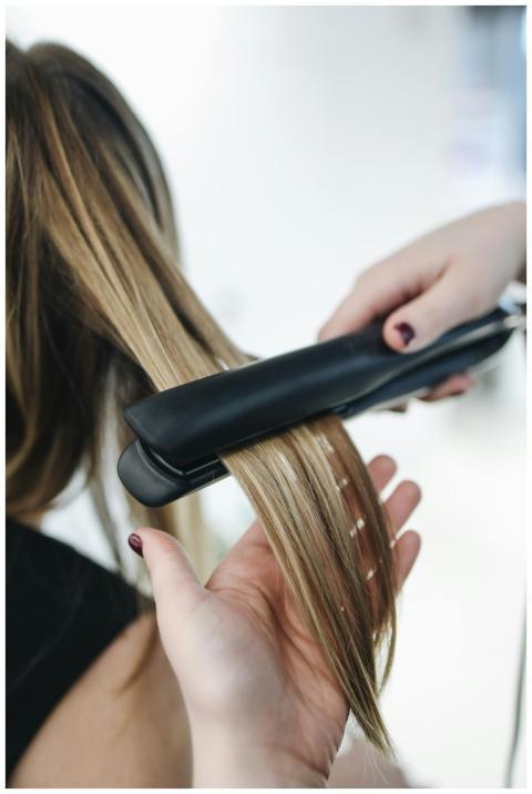 Close-up of a hairstylist using a flat iron on blo