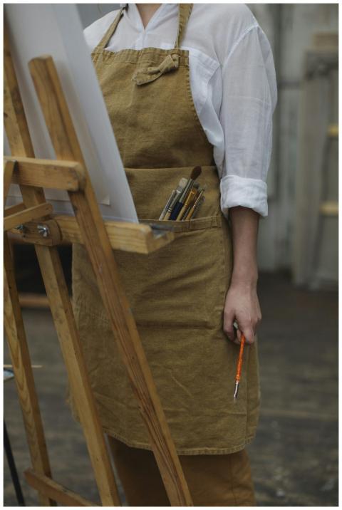 Female artist holds paintbrushes at an easel, crea