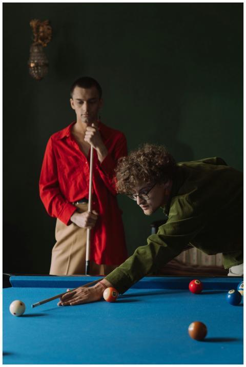 Two men playing billiards on a pool table in a dim