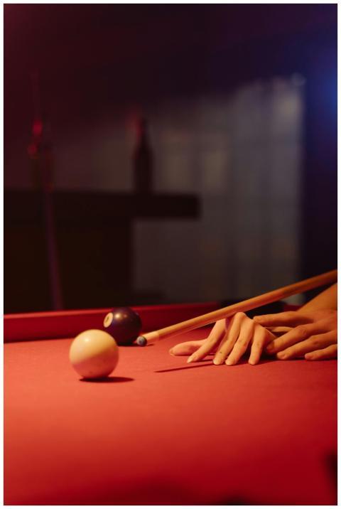 A dimly lit billiards scene focused on hands, cue