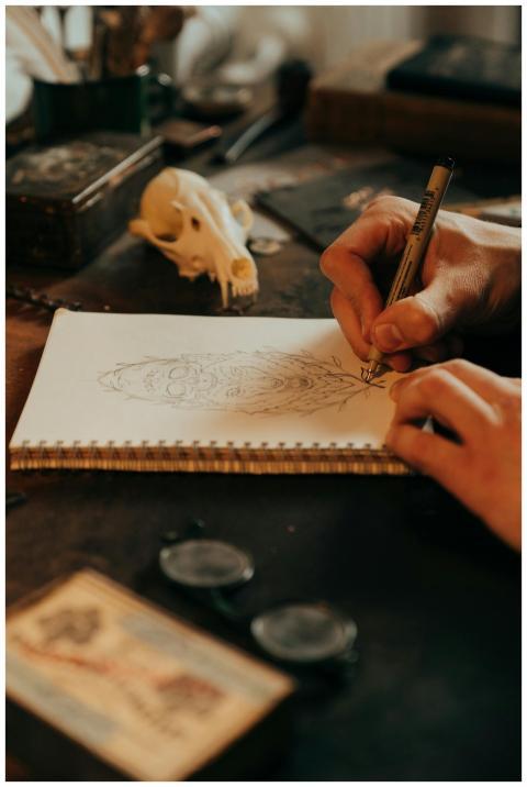 An artist sketches on a notepad at a vintage desk,