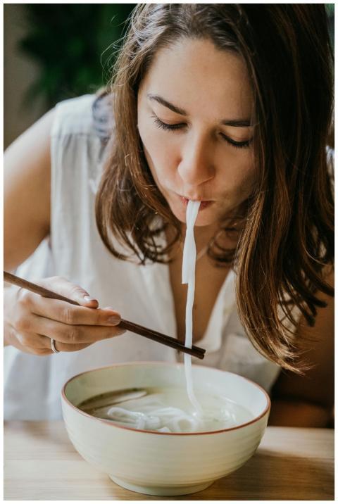 Young woman eating noodle soup with chopsticks in