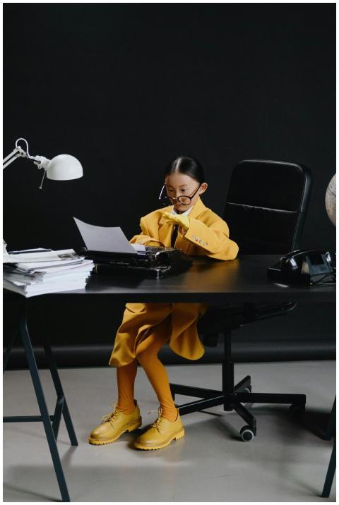 A child in a yellow suit reads documents at a desk