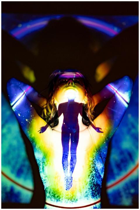 A silhouette emerges through colorful projections,