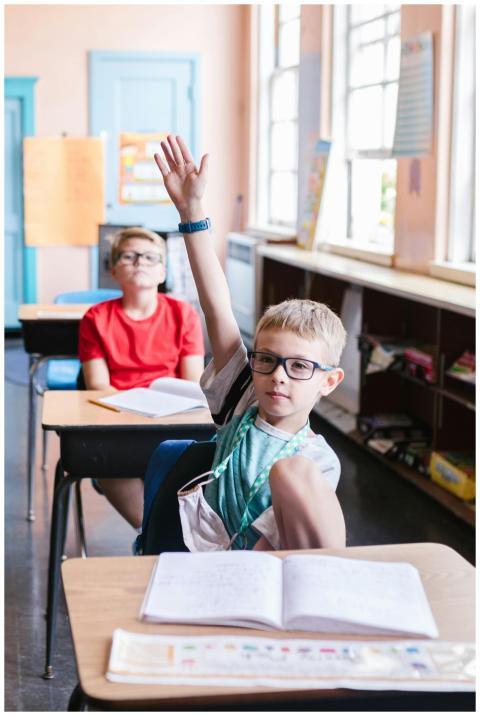Two young boys in an elementary classroom raising