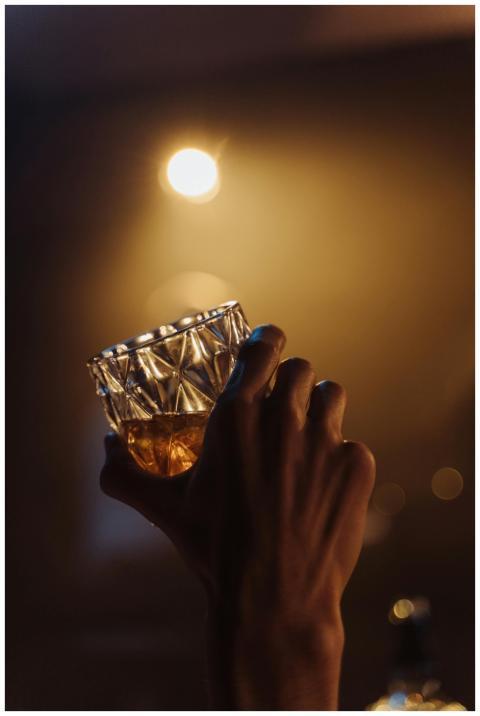 A hand holding a textured glass of whisky, illumin