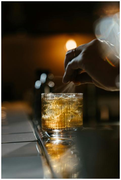 A hand expertly garnishes a whiskey cocktail with